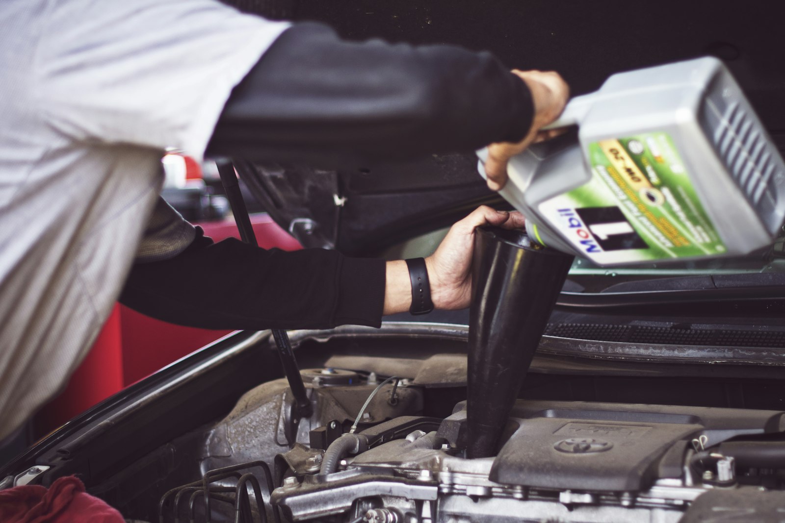 Man doing his own car repair, refilling motor oil